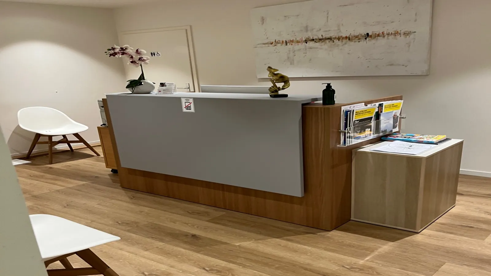 Accueil du centre médical : comptoir de réception en bois, orchidée et chaises blanches